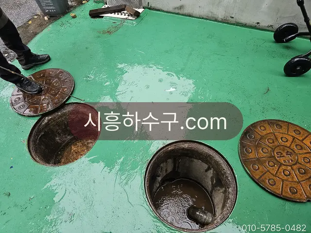 공장 바닥 맨홀 뚜껑을 열고 배관을 점검하는 현장