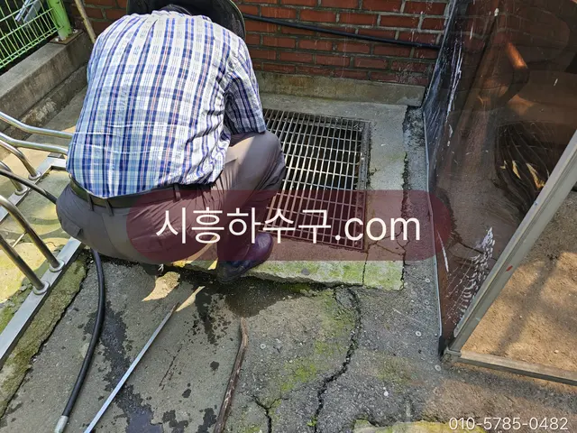 건물 밖 배수구 그레이팅을 열고 막힌 구간을 뚫는 작업